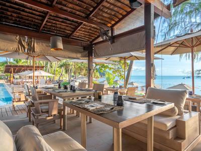 Ristorante aperto sulla spiaggia con tavoli in legno e vista sul mare in una giornata di sole