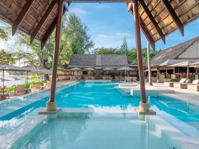 Freiluftpool mit blauer Wasserfläche, Überdachung, Sonnenliegen und Grün im Hintergrund.