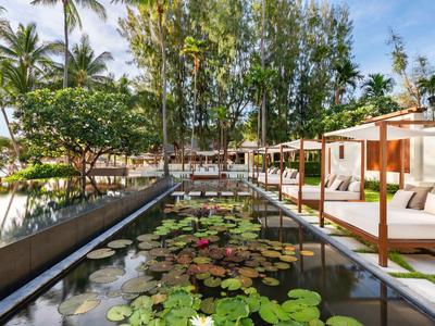 Una zona esterna di lusso con vasca d'acqua, ninfee e comodi lettini sotto le palme.