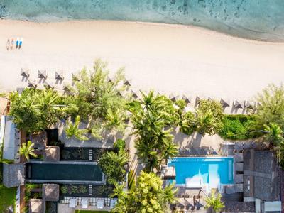 Vista aérea de una playa tropical con palmeras, arena y una piscina cercana al hotel.