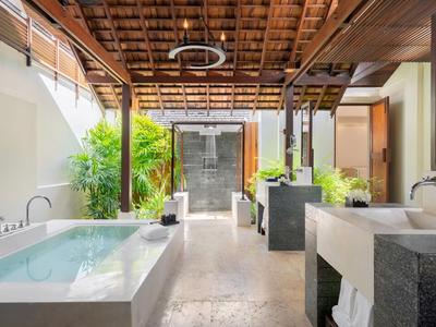 Area bagno aperta con vasca, lavandini e piante sotto un soffitto in legno.