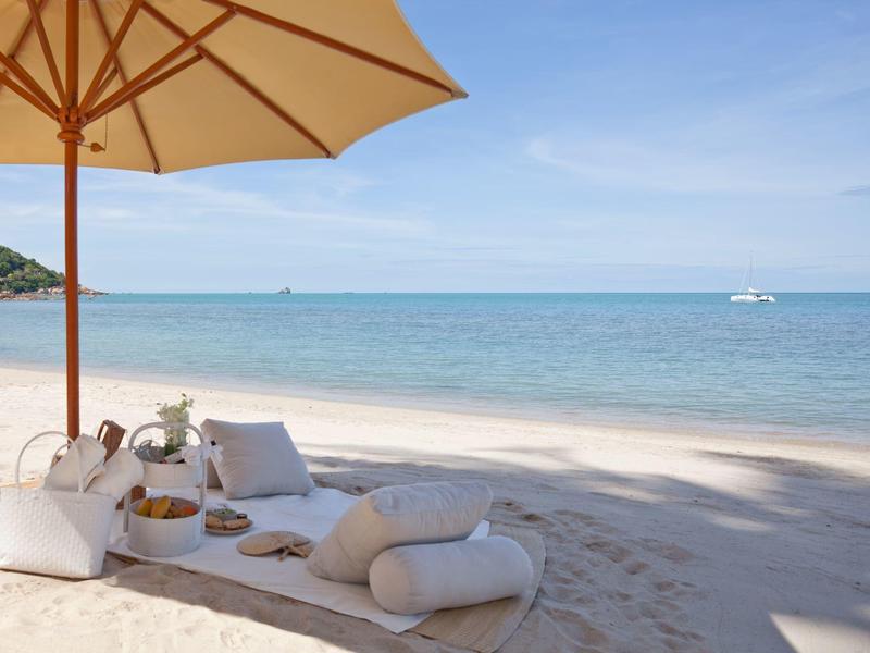 Paisaje relajante de playa con cojines y sombrilla junto al mar tranquilo.