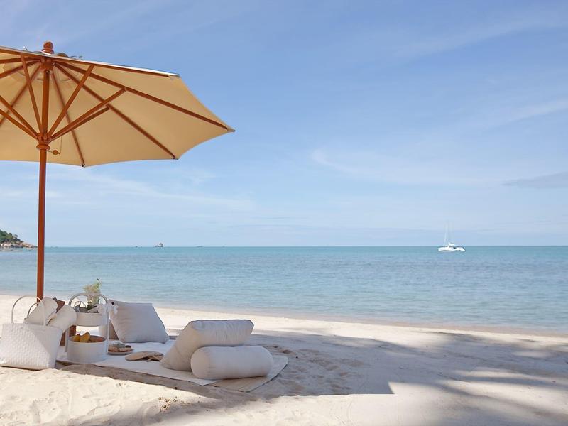 Playa con dos tumbonas bajo una sombrilla y el mar azul al fondo.
