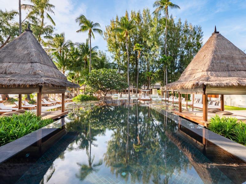 Piscina con dos pavilones de techo de paja y palmeras en un resort tropical.
