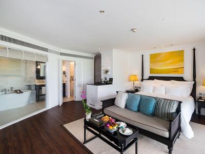 Habitación de hotel moderna con cama doble, sofá, televisor y baño abierto con bañera.