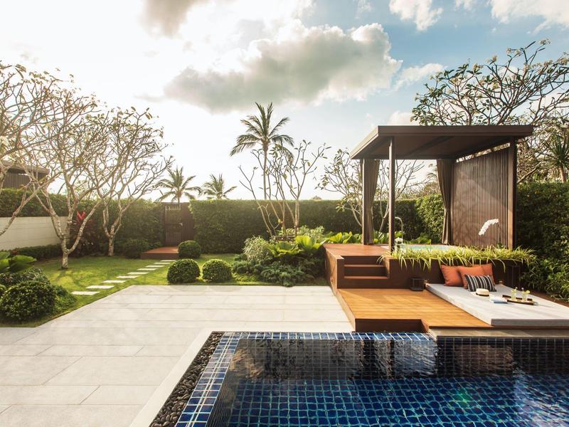 Una atractiva zona de piscina con tumbonas y un área de descanso sombreada en un jardín soleado.