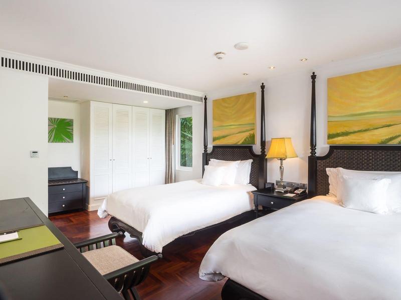 Habitación de hotel moderna con dos camas individuales, colores cálidos y suelo de madera.