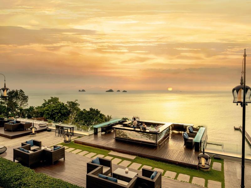 Terraza exterior lujosa con asientos y vista al mar al atardecer.