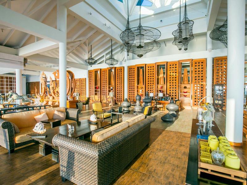 Sala de hotel luminosa con muebles de ratán, suelo de madera y estantes para vinos en la pared.