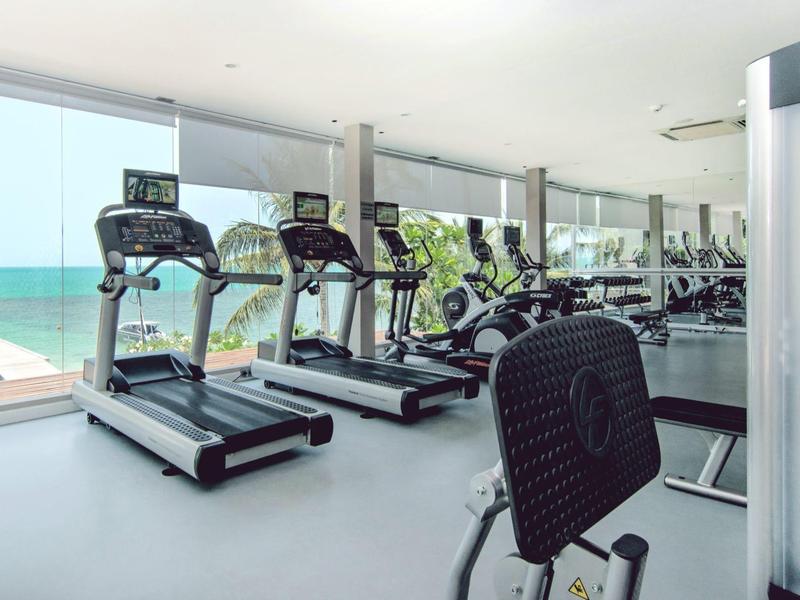 Gimnasio con cintas de correr y vista al mar a través de grandes ventanas.