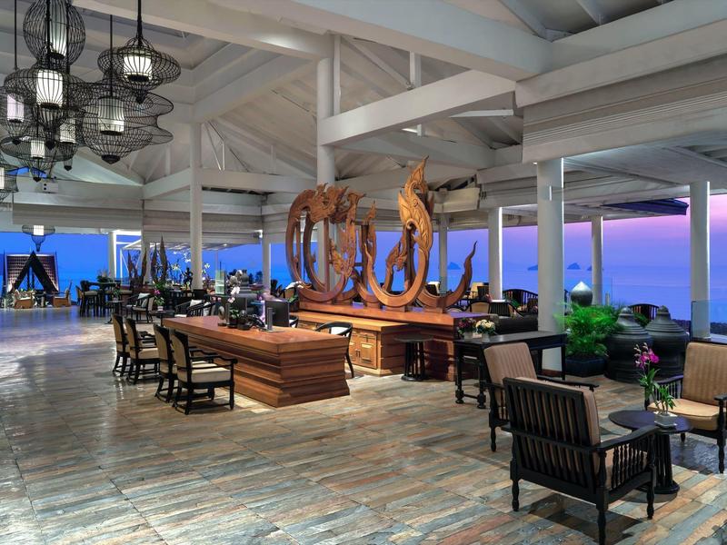 Área de lounge abierta de hotel con muebles de madera elegantes y vista al mar al atardecer.