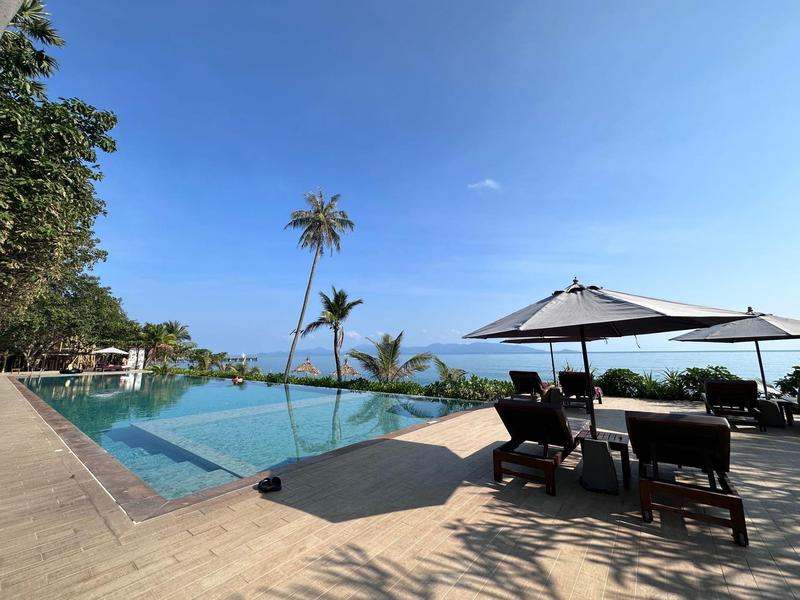 Infinity zwembad met ligstoelen en parasols, palmbomen en blauwe hemel bij zee.