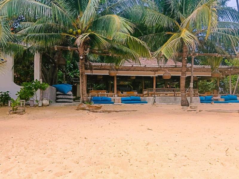 Strandbar met palmbomen, blauwe kussens en zand op de voorgrond