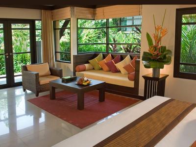 Helles Zimmer mit großem Bett, Sofa, Tisch und grüner Gartenansicht.