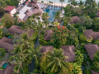 Vista aérea de un resort con bungalows, vegetación exuberante y una piscina junto a la playa.