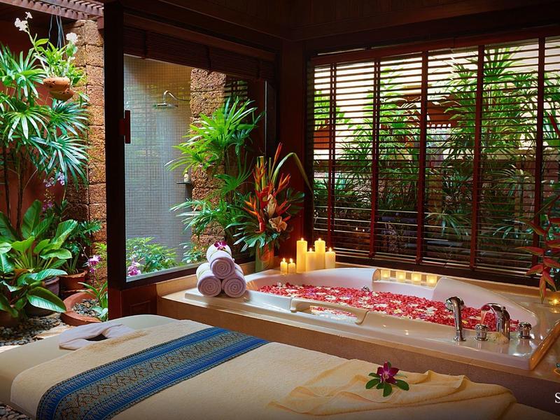 Acogedora sala de spa con jacuzzi, camilla de masaje y luz de velas.