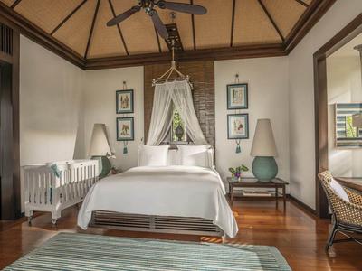 Lichte slaapkamer met hemelbed, rotan stoel en bureau met uitzicht op de tuin.