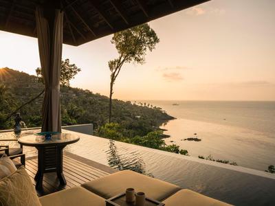 Widok z tarasu na morze o zachodzie słońca z palmami i wzgórzami.