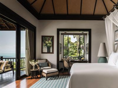 Lichte hotelkamer met tweepersoonsbed, zithoek en balkon met uitzicht op zee.