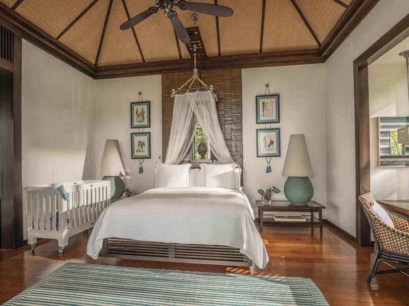 Lichte slaapkamer met hemelbed, rotan stoel en bureau met uitzicht op de tuin.