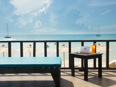 Widok na piaszczystą plażę z parasolami i dwoma żaglówkami z balkonu hotelu.