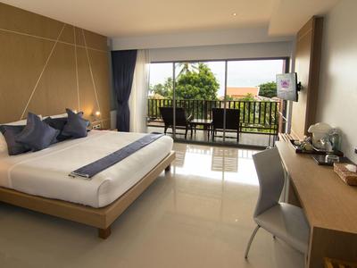 Jasny pokój hotelowy z łóżkiem podwójnym, biurkiem i balkonem z widokiem na zieleń.