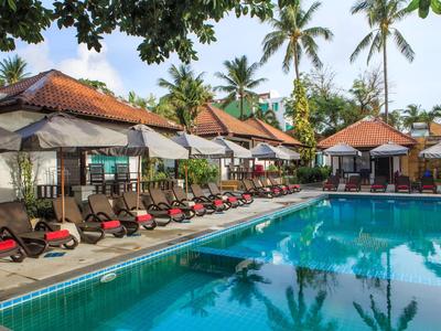 Basen z leżakami i parasolami obok bungalowów i palm pod niebieskim niebem.