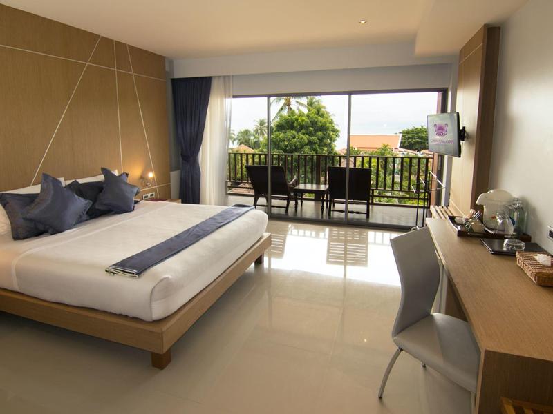 Jasny pokój hotelowy z łóżkiem podwójnym, biurkiem i balkonem z widokiem na zieleń.