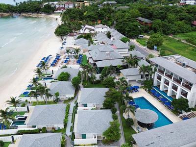 Vista aérea de un resort en la playa con bungalows, piscina y palmeras.