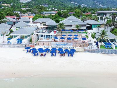 Resort de lujo frente a la playa con varias piscinas y tumbonas azules y blancas en la arena.