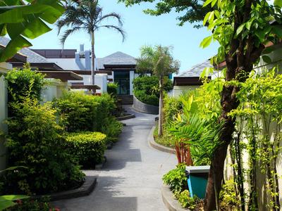Path to a hotel with green plants and small buildings on a sunny day.