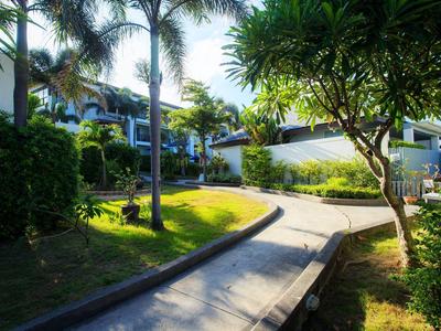 Un camino con palmeras y césped verde en un jardín tropical de hotel bajo la luz del sol.