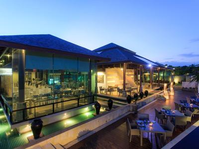 Modern hotel restaurant with indoor and outdoor seating at dusk, illuminated pool in foreground.