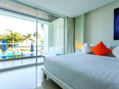 Habitación de hotel luminosa con cama grande y vista a la piscina y palmeras a través de una pared de vidrio.