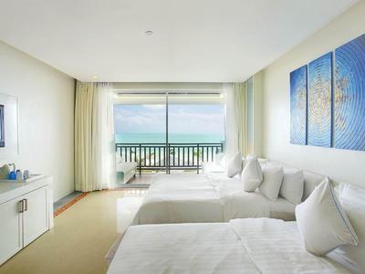 Habitación de hotel luminosa con camas dobles, balcón con vistas al mar y mobiliario moderno.