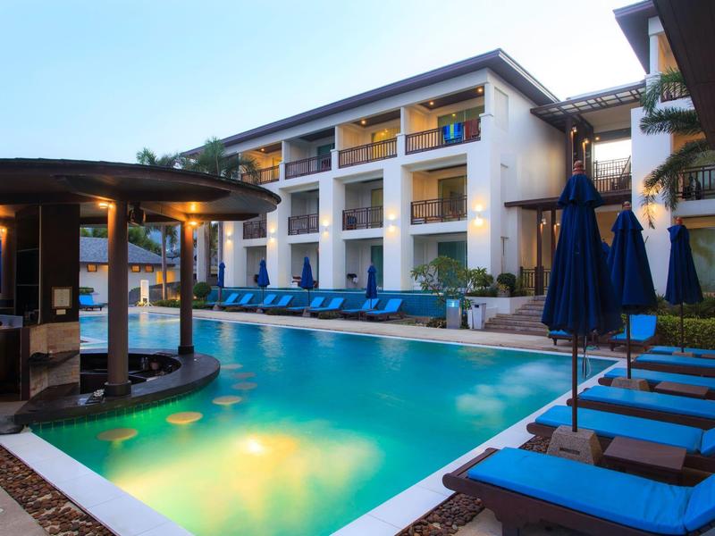 Piscina moderna de hotel con tumbonas azules y zona cubierta al atardecer.