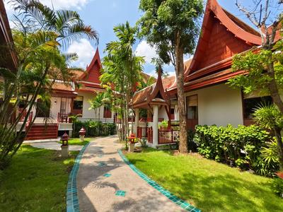 Pad door tropische tuin naar traditionele Thaise huizen met rode daken onder blauwe lucht.