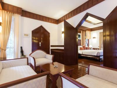 Chambre d'hôtel lumineuse avec fauteuils blancs, murs en bois et chambre adjacente.
