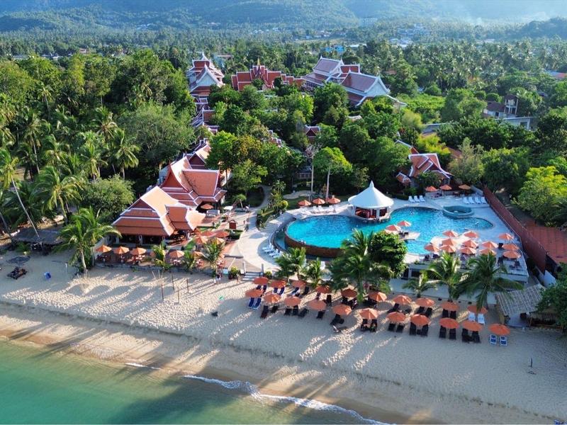 Vue d'ensemble d'un complexe tropical avec piscine, plage et de nombreuses chaises longues au bord de la mer.