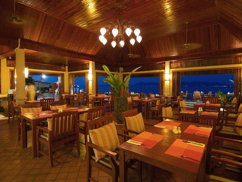 Restaurant chaleureux avec mobilier en bois et vue sur la mer au crépuscule.