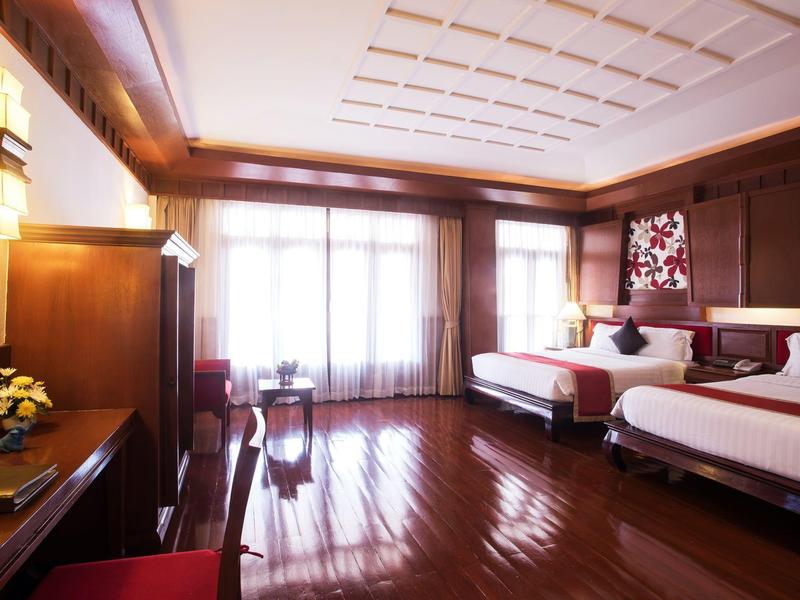 Chambre d'hôtel spacieuse avec sols en bois, deux lits et grandes fenêtres laissant entrer beaucoup de lumière naturelle.