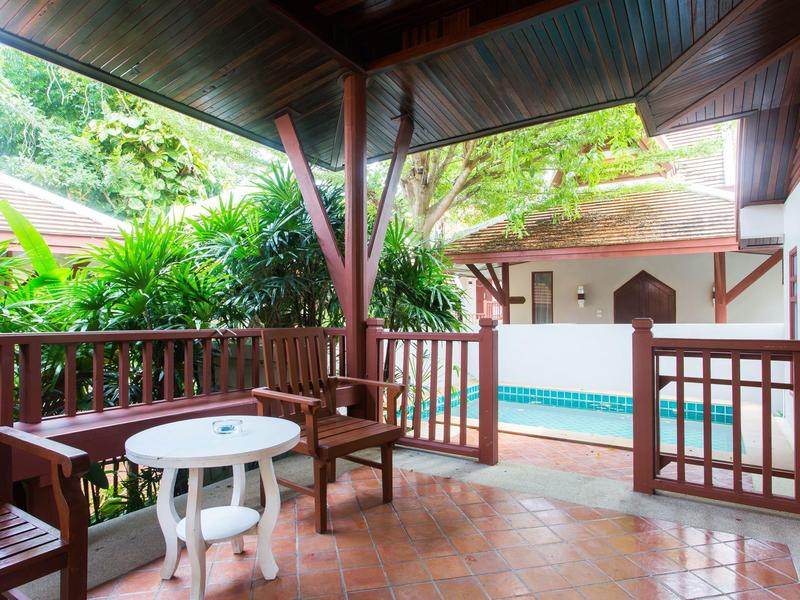 Terrasse couverte avec mobilier en bois donnant sur une piscine et des plantes vertes.