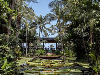 Giardino tropicale con ninfee, palme e un percorso in legno verso un lounge aperto