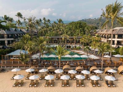 Resort sulla spiaggia con file di ombrelloni, lettini, piscina e palme sullo sfondo.