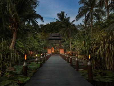 Sentiero in legno illuminato che conduce a un ingresso tra palme tropicali al crepuscolo.