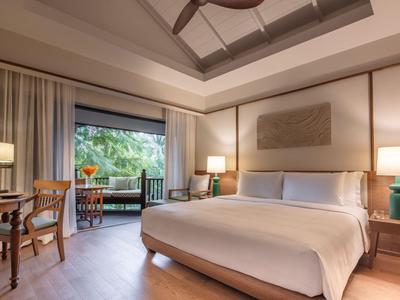 Camera d'hotel moderna con letto grande, scrivania e balcone con vista sul verde.