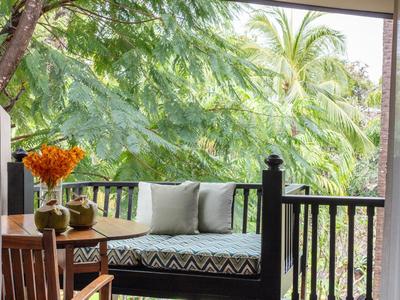 Veranda accogliente con panca in legno e cuscini, vista su piante verdi rigogliose e palme.