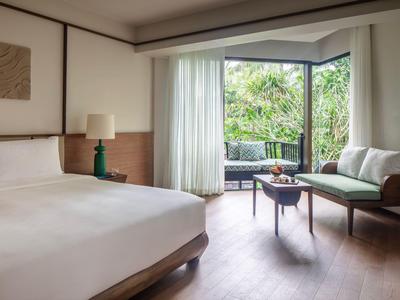 Camera d'hotel luminosa con letto grande, divano, tavolo e balcone con vista sul verde.