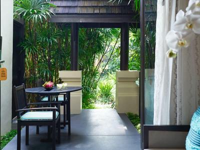 Vista attraverso una porta a vetri aperta su una terrazza con posti a sedere e vegetazione rigogliosa sullo sfondo.