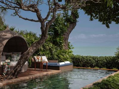 Piscina moderna con comodi lettini e vista mare in un giardino tropicale.